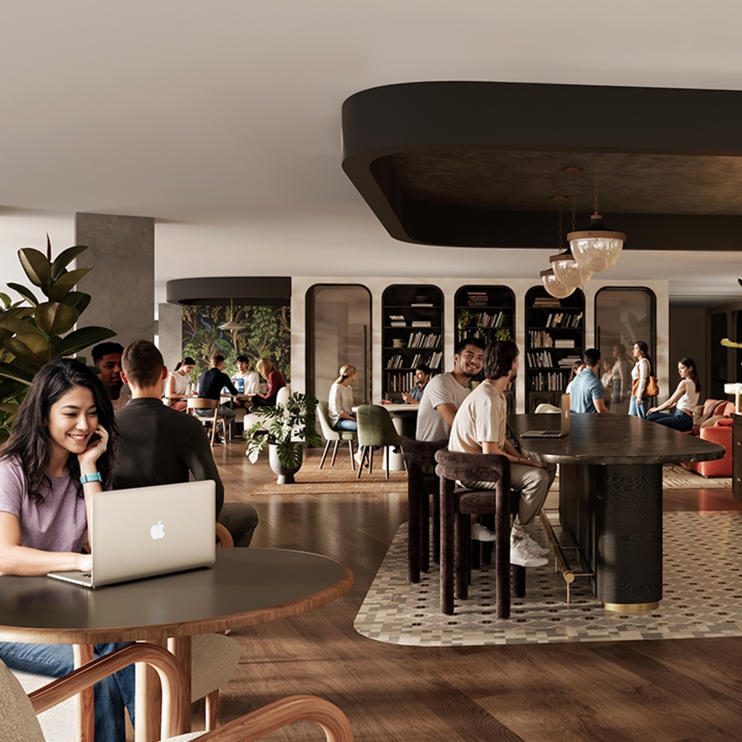 A modern, spacious coworking space ideal for Purdue off campus housing residents, with people working on laptops, reading, and chatting. Wooden floors, large tables, bookshelves, and green plants create a relaxed, collaborative atmosphere.