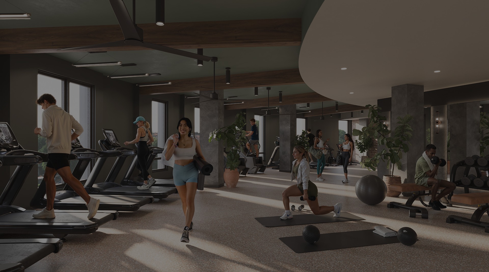A modern gym in Purdue off campus housing with people working out: some are using treadmills, others lifting weights, stretching, or exercising on mats. The space is bright with large windows, plants, and contemporary decor.