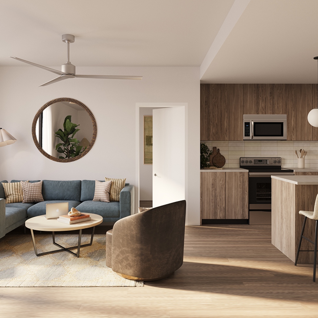 Modern living room and kitchen with wooden floors, a blue sectional sofa, a round coffee table, a brown chair, and a large wall mirror. The kitchen features wood cabinets and stainless steel appliances.