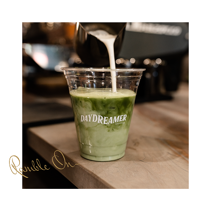 A barista pours milk into a clear plastic cup of iced matcha latte labeled “Daydreamer” on a café counter near Purdue off campus housing.