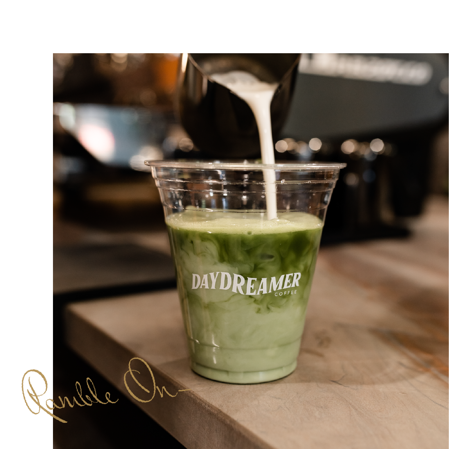 A barista pours creamy milk into a clear cup of iced matcha latte at DAYDREAMER COFFEE, perfect for Purdue off campus housing students. The phrase Ramble On is scripted in the lower left corner.
