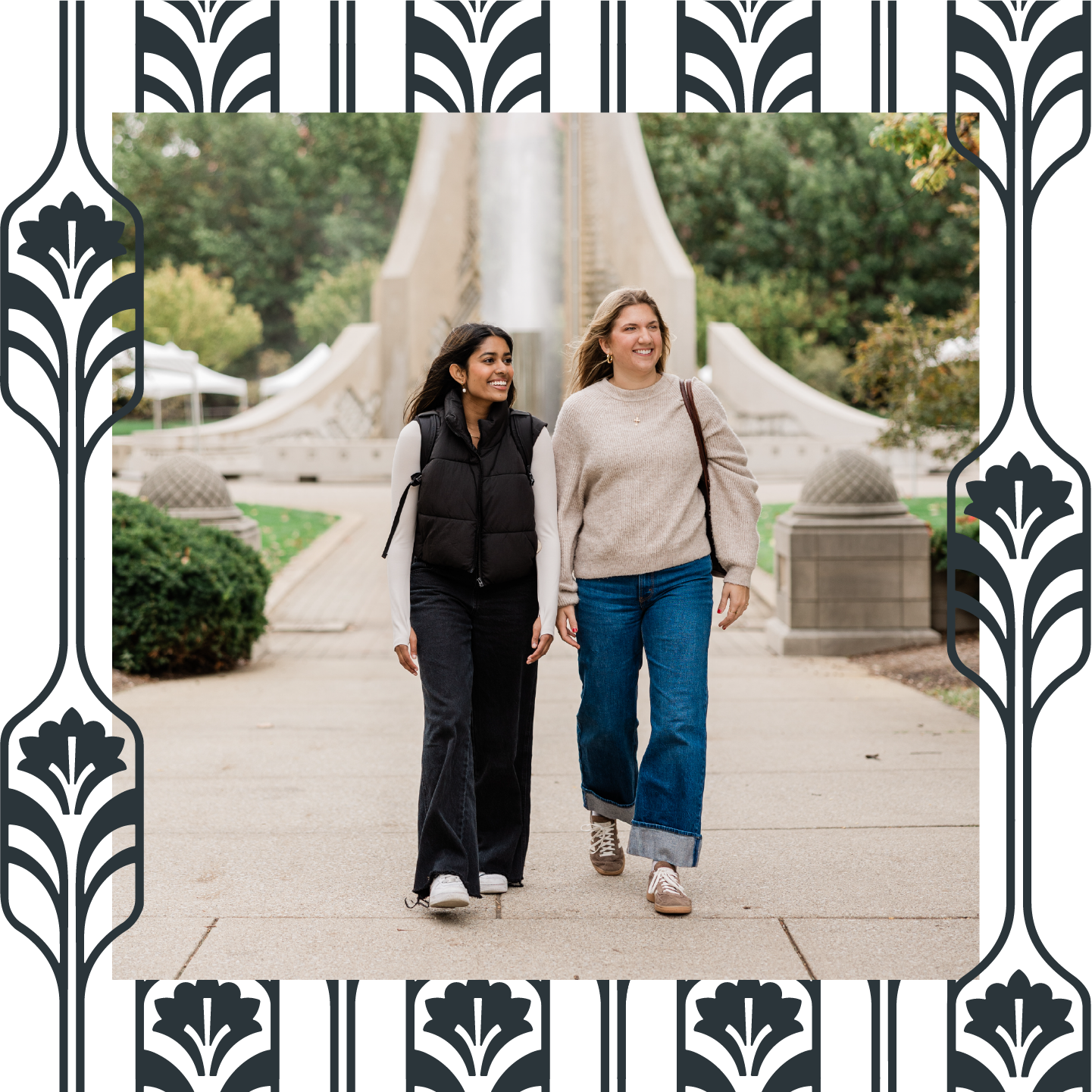 Two women walk side by side, smiling, on a paved path lined with greenery and a large fountain—perfectly capturing the vibrant lifestyle near apartments in West Lafayette. The image is framed with a black and white decorative border.