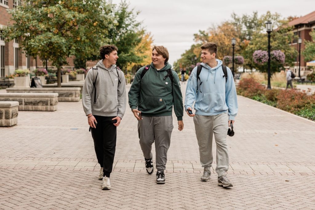 Three Purdue students wearing backpacks walking together in West Lafayette, smiling and chatting as they head to class.
