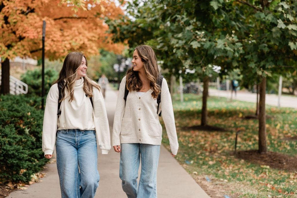 Two Purdue University students with backpacks walking side by side and talking together outside at Rambler Riverfront.