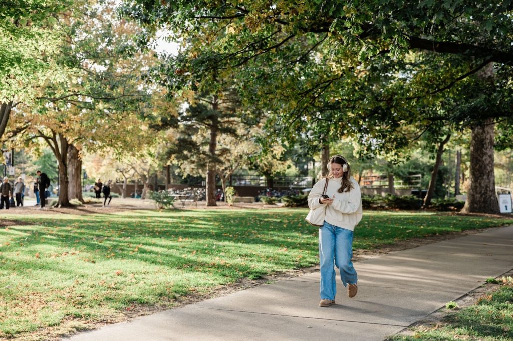 Purdue Student walking on campus listening to music on her phone.