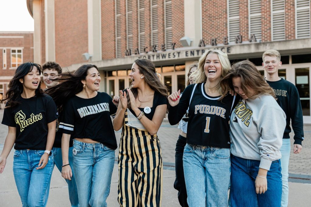 A group of Purdue University students wearing Purdue-branded clothing, walking and laughing together outdoors.