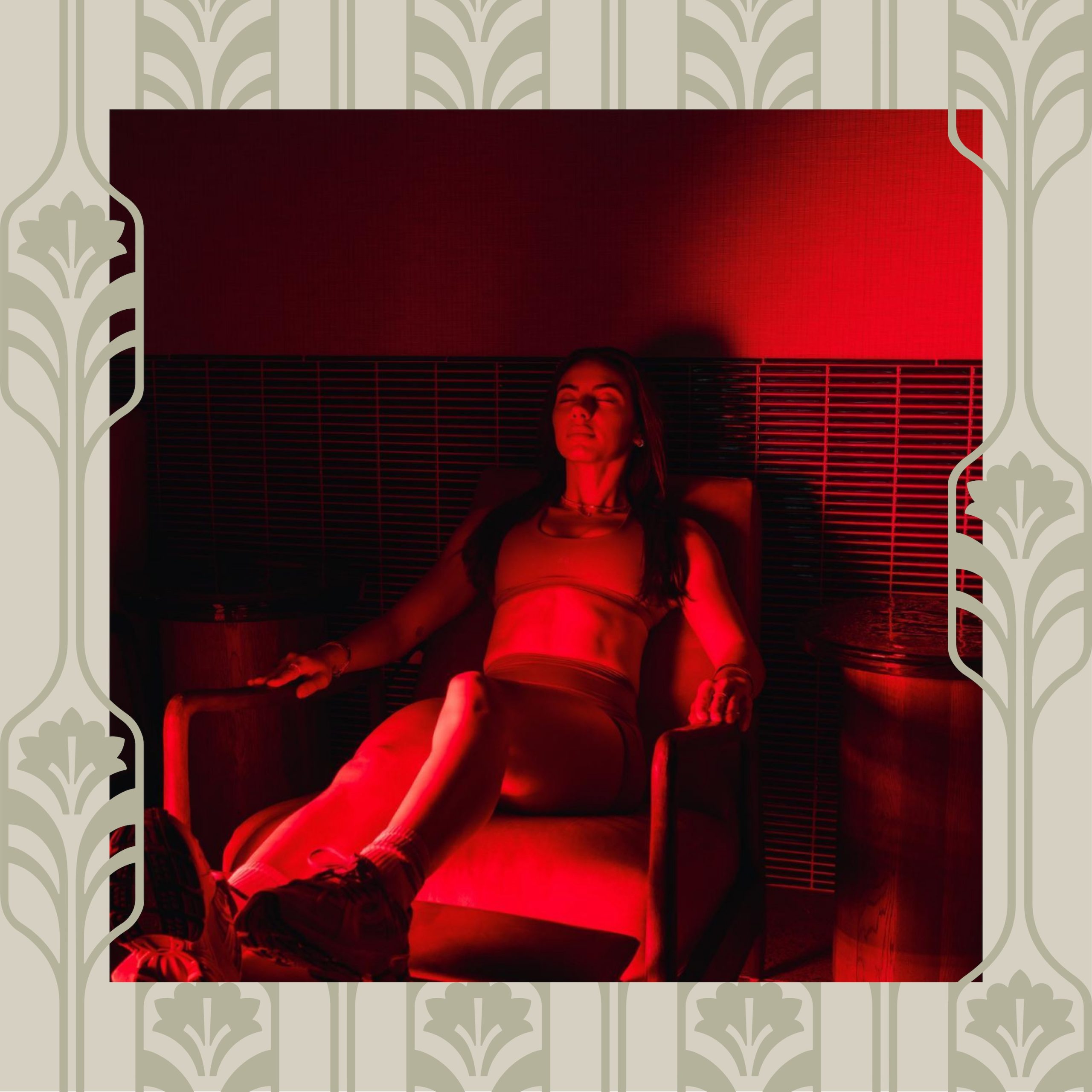 A woman in athletic wear sits relaxed in a chair, bathed in dramatic red lighting, with a patterned wallpaper border framing the image—capturing the unique vibe of Purdue off campus housing.