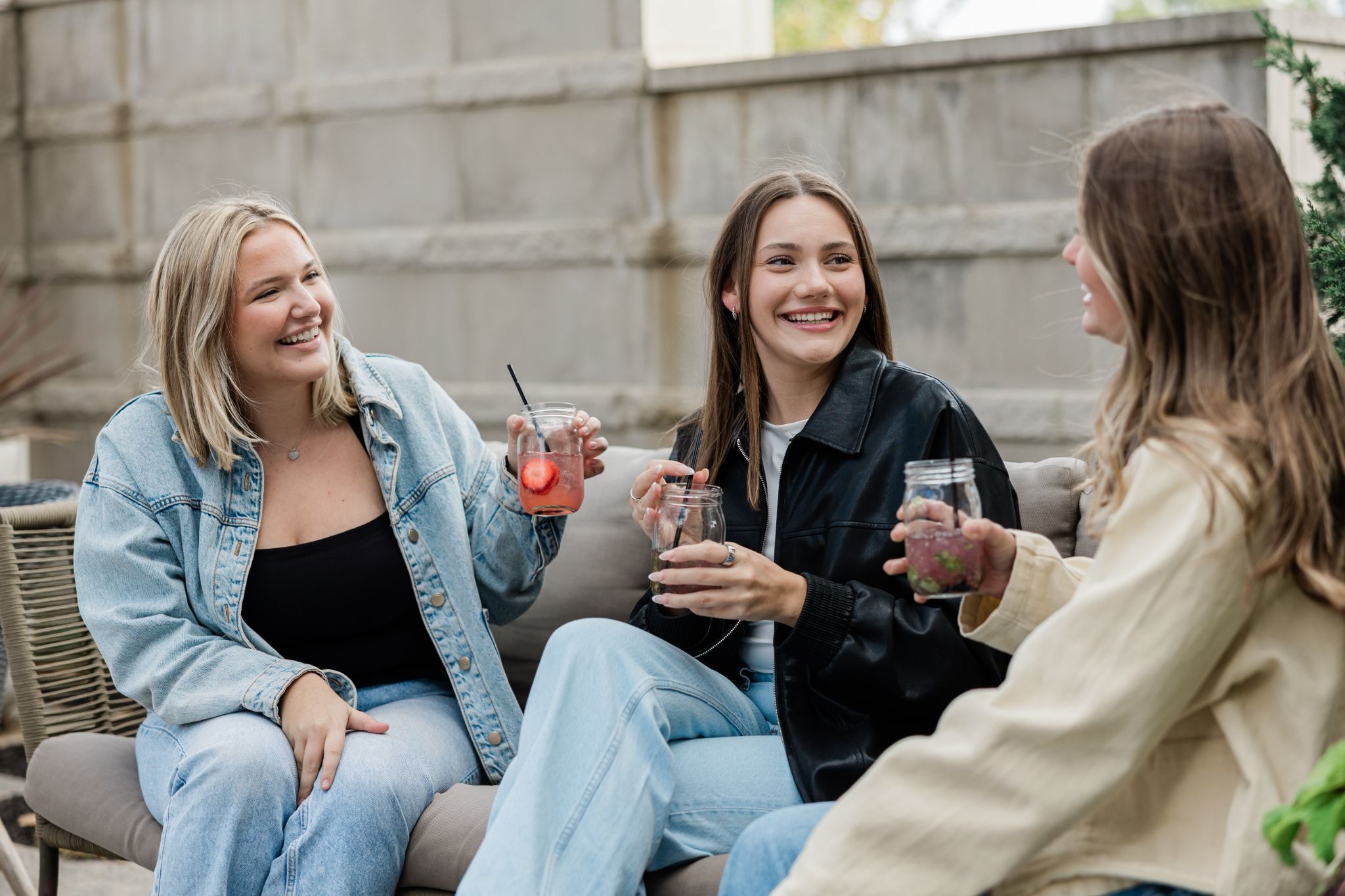 Three Purdue students sitting together, chatting and smiling while holding drinks.