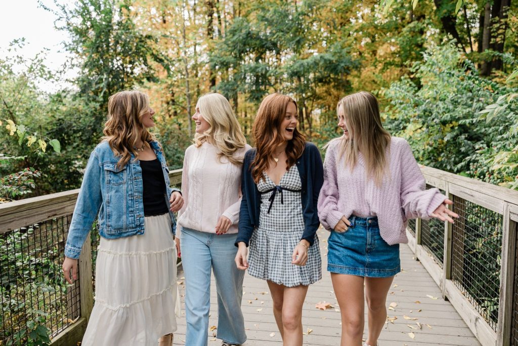 Four girls walk together across a bridge in the forest, talking and enjoying the scenery.