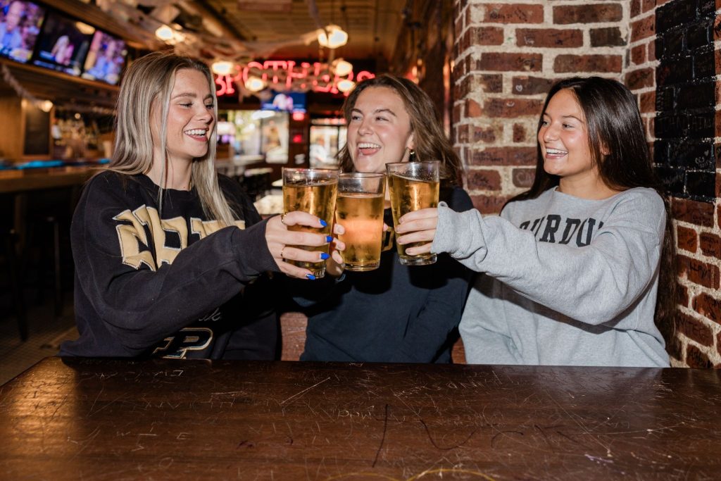 Purdue students at a bar smiling and clinking their drinks together in a cheerful toast.