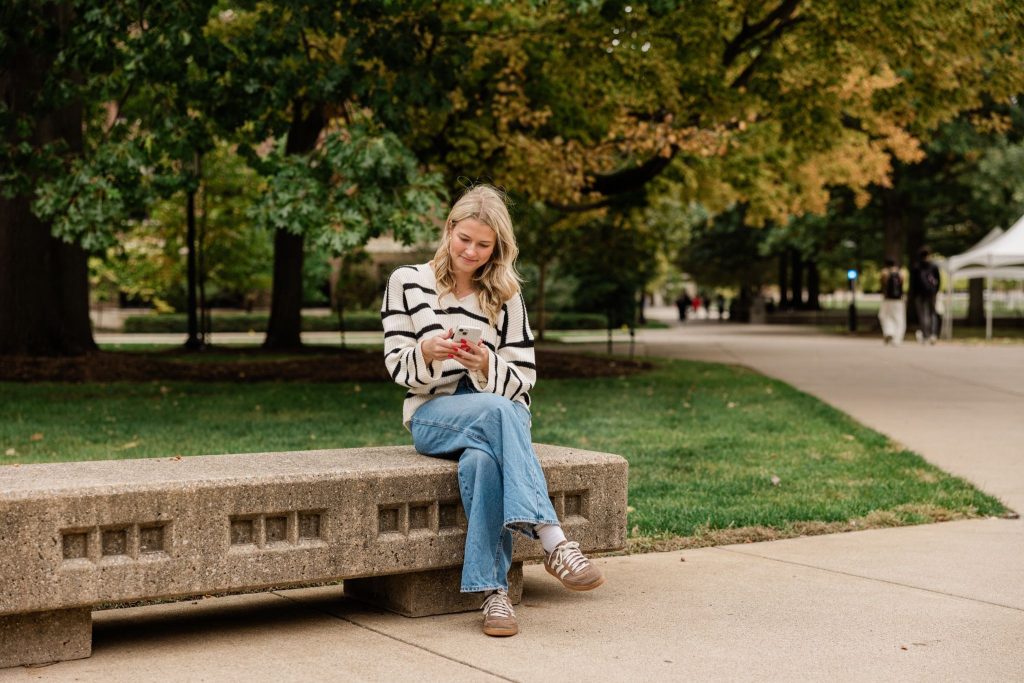 Purdue student sitting on a bench on their phone on Purdue’s campus.