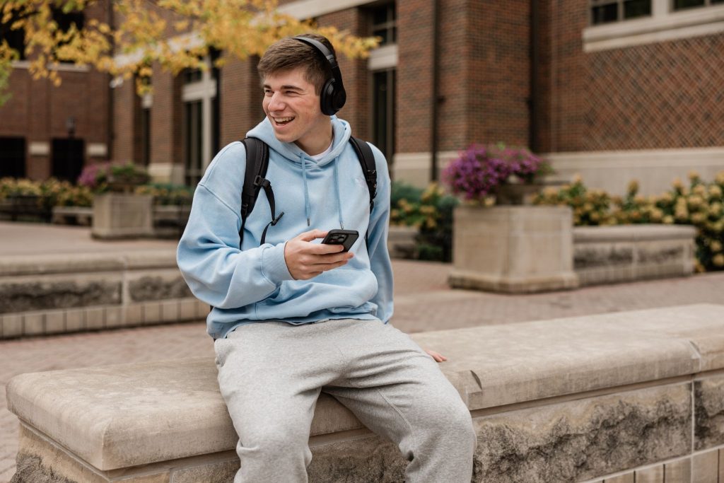 Purdue student sitting on a bench on campus listening to music.